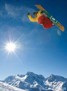A snowboarder performing a stunt spinning over mountain peaks at Sainte Foy, France